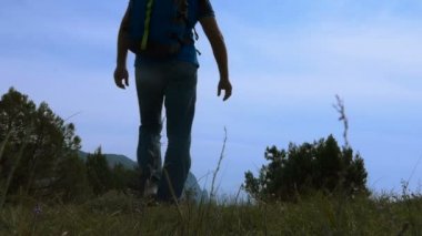 Yüksek bir dağ deniz gökyüzü üzerinde değer sırt çantası ile güneş gözlüklü bir adam. Deniz manzarası izlerken yüksek bir dağın üzerinde genç bir adam. Yaz parlak güneşli bir gün.