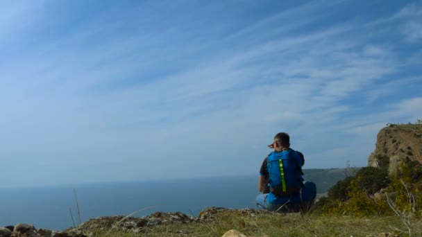 Человек Солнечных Очках Рюкзаком Сидит Высоко Горе Над Морем Против — стоковое видео
