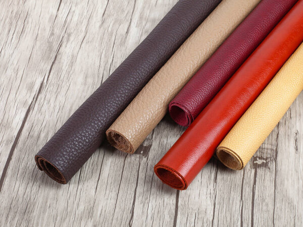 Rolled up different colors natural leather textures samples on light wooden background.