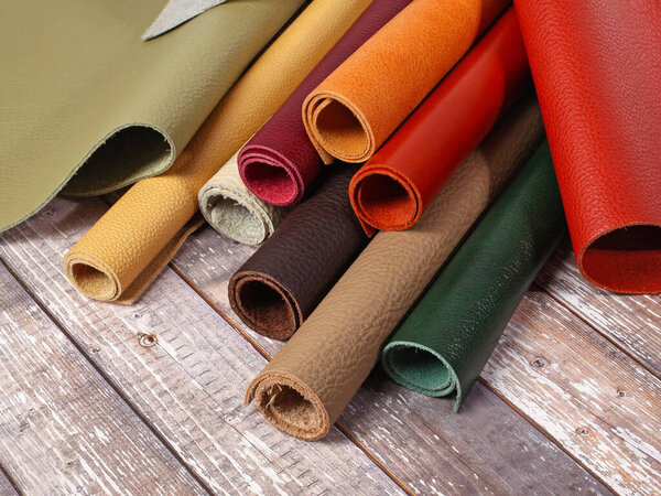 Rolled up different colors natural leather textures samples on light wooden background