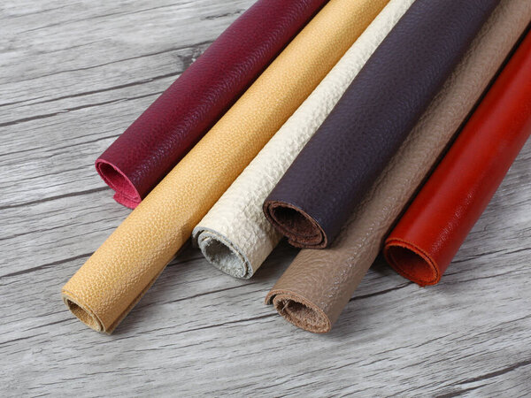 Rolled up different colors natural leather textures samples on light wooden background