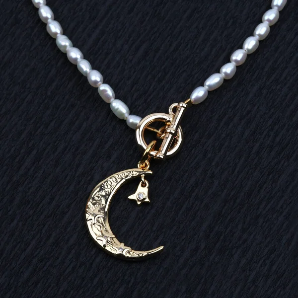 Golden crescent moon pendant with pearl necklace on black textured background