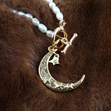 Kahverengi kürk arka planında inci kolyesi olan altın hilal bir kolye.