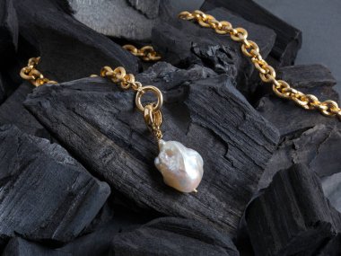 Siyah kömür zemininde beyaz barok inci kolyesi olan altın zincir. Yakın çekim.