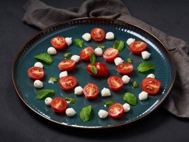 Nane yapraklı mozzarella peyniri ve yeşil mavi tabakta domates, gri masada.                               