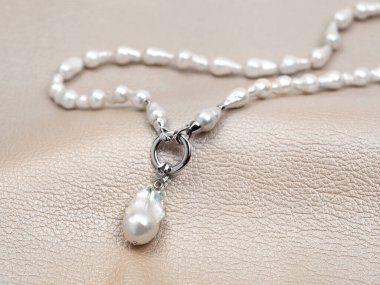 Beyaz barok inci kolye ve bej rengi deri arka plan.