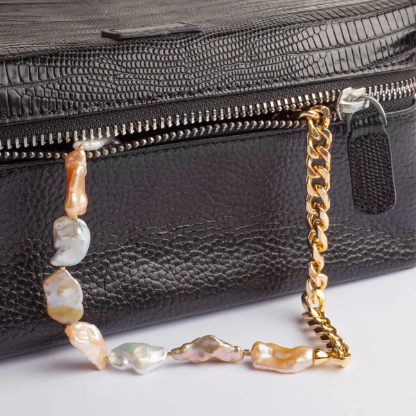 Women`s baroque pearl chain necklace with female black leather cosmetic bag. Close-up shot