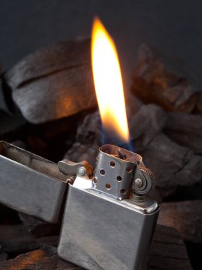 Koyu kömür arka planında yanan ateşle metal gaz çakmağının yakın plan yansımaları