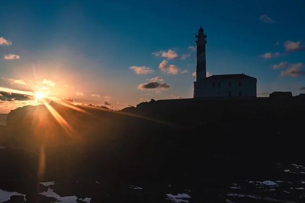 İspanya, Menorca 'da bulutlu gökyüzü ile kış günü şafak vaktinde güneş patlamaları olan deniz feneri