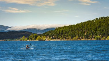 Genç atletik adam kanosuyla Aguilar barajının sakinliğinin tadını çıkarıyor. Palencia, İspanya.