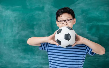 Gülen öğrenci elinde futbol topu tutuyor. 