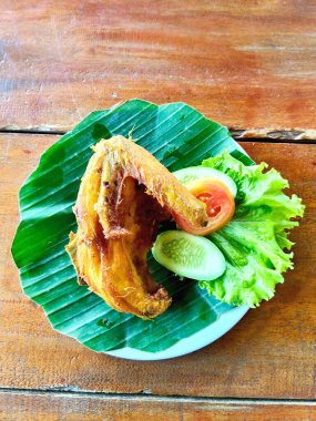 Bir tabak kızarmış tavuk kanadı yanında bir kepçe beyaz pirinç ve taze Endonezya Sundan salatası, ya da muz yaprağı üzerinde Lalapan..