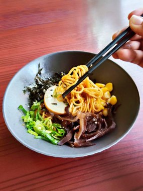 Bir el, lezzetli bir Japon kuru rameninden bir yığın erişte kaldırmak için çubuk kullanıyor.).