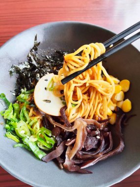 Bir el, lezzetli bir Japon kuru rameninden bir yığın erişte kaldırmak için çubuk kullanıyor.).