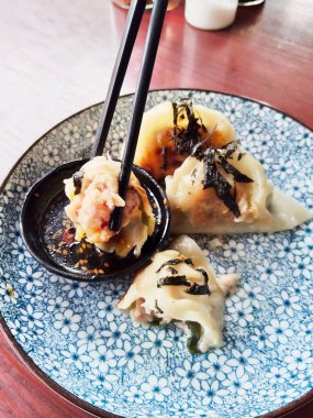 Nori ve susam tohumlarıyla süslenmiş altın, çıtır gyoza hamur tatlısı, güzel mavi ve beyaz bir tabakta servis edilir..