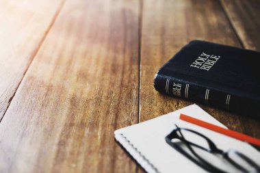 Kutsal İncil 'i kapat ve not defterini kalem ve gözlüklerle ahşap masaya koy.