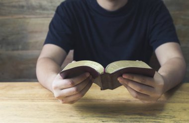 Bir adamın el ele tutuşması ve kutsal İncil 'i ahşap masada okuması. Kopya alanı olan Hıristiyan arka planı.