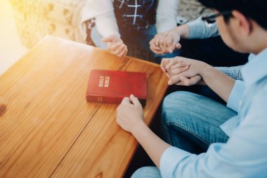 Hıristiyan küçük bir grup el ele tutuşup ahşap bir masanın etrafında dua ediyor ve İncil 'i ahşap bir masaya koyuyor.