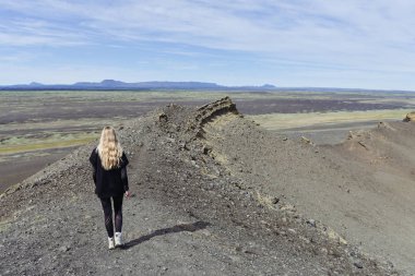 One of the crater landscape on the North-East of Iceland. Young woman traveller walking on the top of the crater clipart