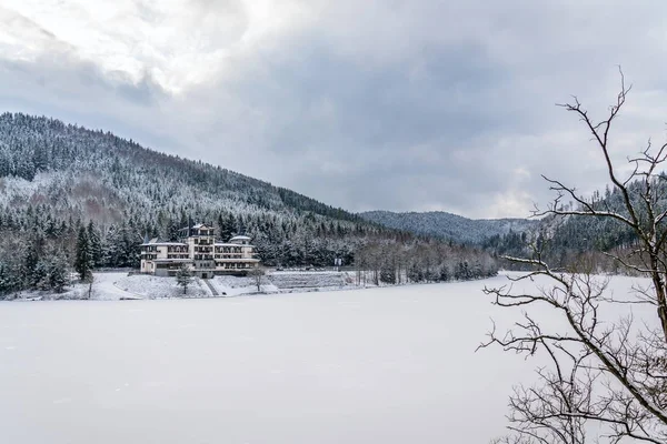 Solitary building in beautiful snowy winter forest landscape, frozen Brezova dam, Shining movie style