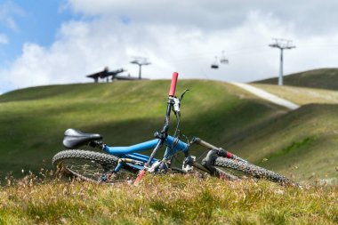 Zeminde yatan tam süspansiyon yokuş aşağı dağ bisikleti, arka planda cableway ile Livigno üzerinde dağlar, güneşli yaz günü, İtalya