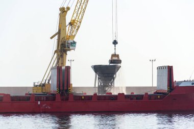 Limandaki büyük yük gemisinden kum boşaltan sarı vinç, nakliye verimliliği, kum kıtlığı konsepti, güneşli gün fotokopi alanı