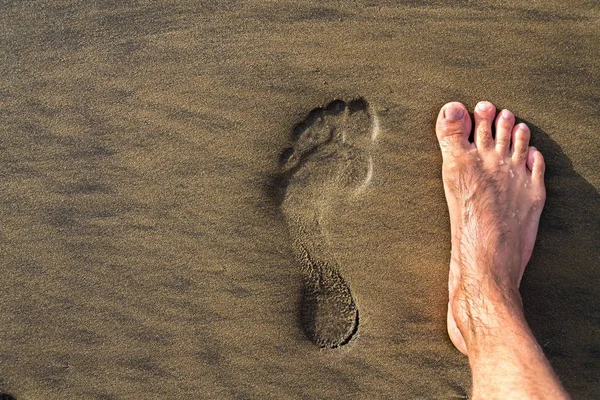 Human footprint with barefoot feet in brown yellow sand beach background, active healthy living and personal growth concept, copy space