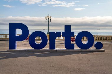 Sahil ve sahil boyunca gezinti güvertesinde mavi üç boyutlu Porto işareti, Portekiz, güneşli yaz gününde gün batımı