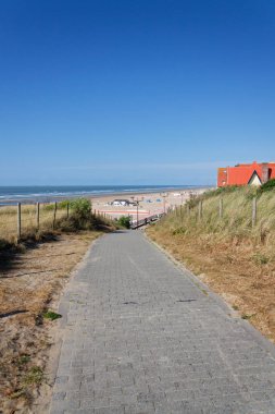 Kum tepelerinin yakınındaki güzel kumsaldaki insanlar Batı Flanders, güneşli yaz günü 23 Mayıs 2025, De Haan, Belçika.