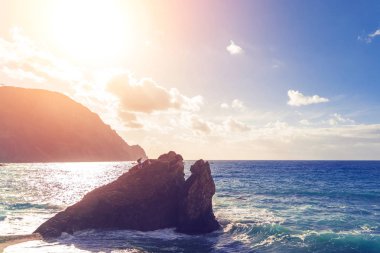 Üç çocuklu bir kayaya deniz günbatımı sırasında ayakta adam