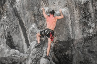 Genç erkek dağcı sigortası olmadan kayalık bir duvara tırmanıyor.