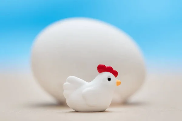 Little toy chicken near the big white egg on a blue background