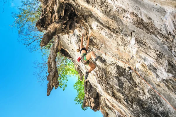 Young woman climbs on a overhanging cliff on a summer day