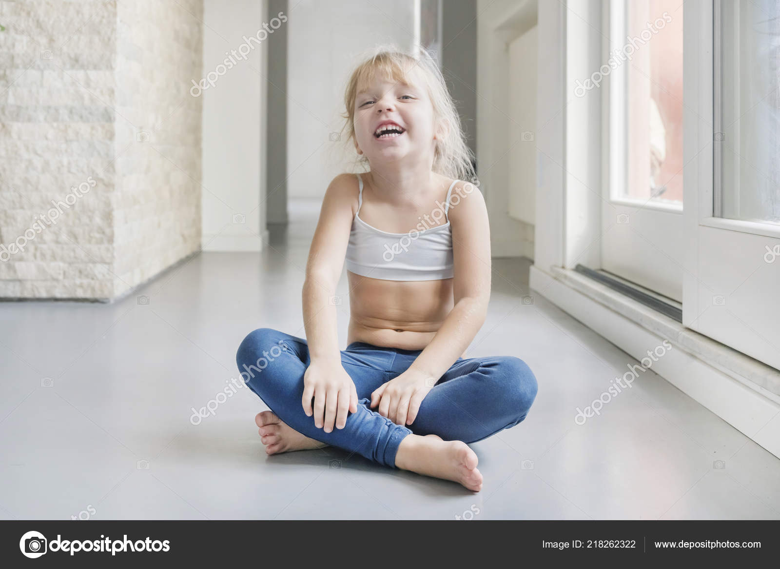 Smiling Little Blond Girl White Top Blue Leggings Sitting Floor Stock Photo  by ©watman 218262322