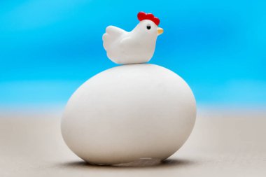 Bir büyük beyaz yumurta mavi bir arka plan üzerinde oturan küçük oyuncak tavuk