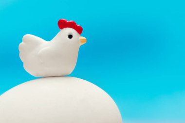 Bir büyük beyaz yumurta mavi bir arka plan üzerinde oturan küçük oyuncak tavuk
