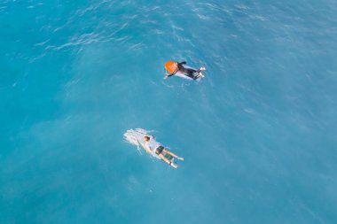 Suda bir sörf tahtası üzerinde iki sörfçü, üst görünümü