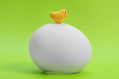 Bir büyük beyaz yumurta yeşil bir arka plan üzerinde oturan küçük oyuncak sarı civciv 