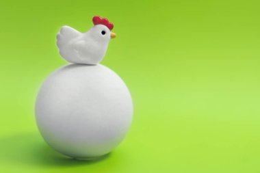 Bir büyük beyaz yumurta yeşil bir arka plan üzerinde oturan küçük oyuncak tavuk