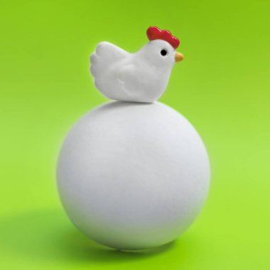 Bir büyük beyaz yumurta yeşil bir arka plan üzerinde oturan küçük oyuncak tavuk 