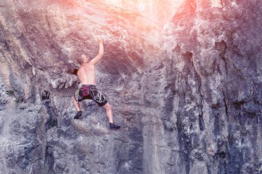 Genç bir erkek dağcı güneşli bir günde uçuruma tırmanır.