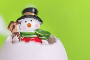 Yeşil bir arka plan üzerinde yumurta kabuğu içinde küçük oyuncak kardan adam