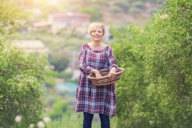 Elinde hasır sepet ile bahçede duran damalı elbisegüzel genç sarışın kadın