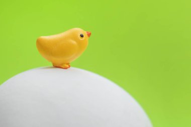 Bir büyük beyaz yumurta yeşil bir arka plan üzerinde oturan küçük oyuncak sarı civciv  