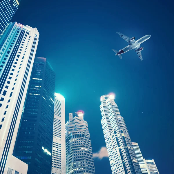 Airplane flying over skyscrapers at night