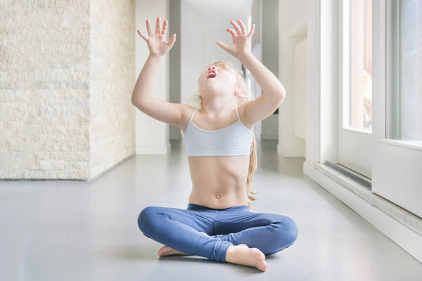 Маленькая блондинка, занимающаяся йогой в комнате
