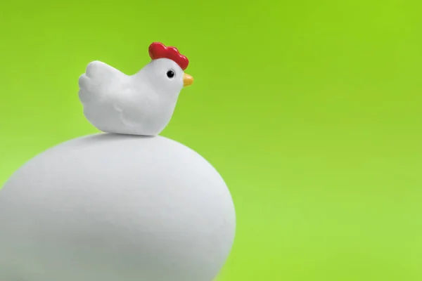 Little toy chicken sitting on a large white egg on a green background