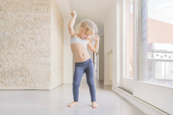 Маленькая блондинка танцует в солнечной комнате возле окна
