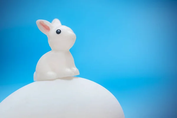 Маленький Белый Игрушечный Кролик Сидит Большом Белом Яйце Синем Фоне — стоковое фото