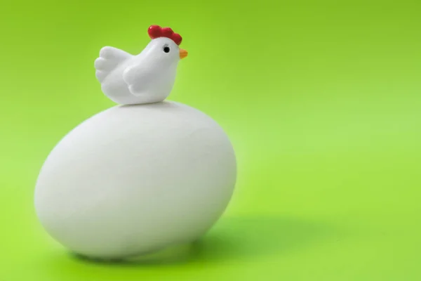 Little toy chicken sits on a big egg on a green background